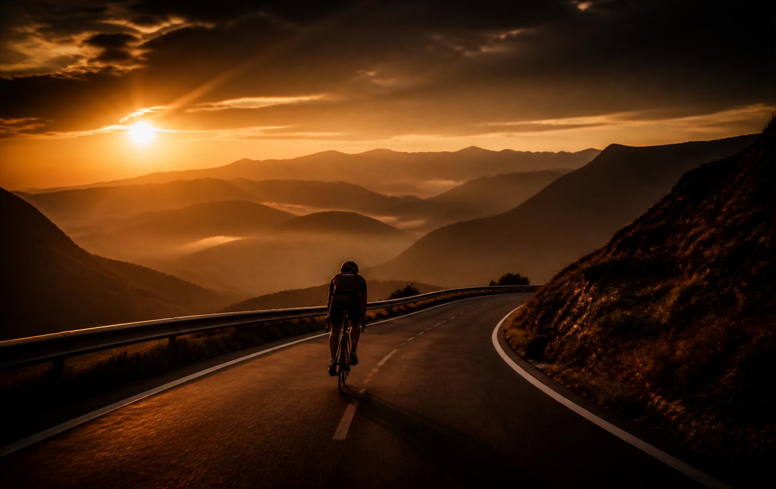 Silhouette of a cyclist descending a mountain road at dusk